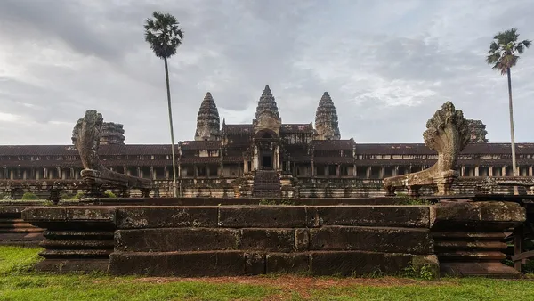 Pięć wież świątyni Angkor Wat na tle pochmurnego nieba, z palmami po bokach