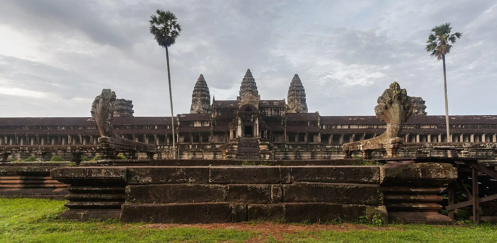 Pięć wież świątyni Angkor Wat na tle pochmurnego nieba, z palmami po bokach