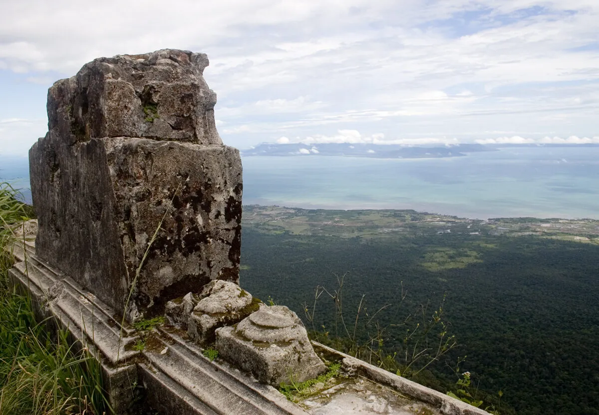 Widok ze szczytu Phnom Bokor na zalesione równiny i wybrzeże, na pierwszym planie kamienne ruiny