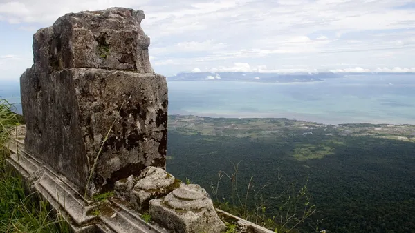 Widok ze szczytu Phnom Bokor na zalesione równiny i wybrzeże, na pierwszym planie kamienne ruiny