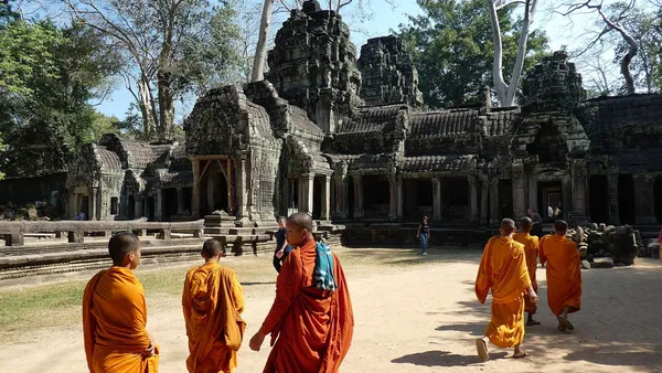 Mnisi w szafranowych i pomarańczowych szatach idą przez dziedziniec świątyni Ta Prohm w Angkorze