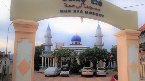 Brama z napisem Muk Dac Mosque, a za nią meczet z niebieską kopułą i dwoma minaretami w dzielnicy Chroy Changvar w Phnom Penh