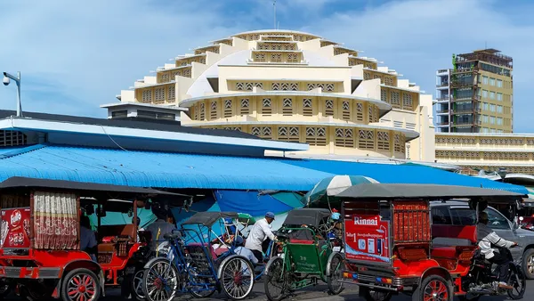 Żółta kopuła hali Central Market w Phnom Penh, przed nią tuk-tuki i riksze pod niebieskim zadaszeniem straganów