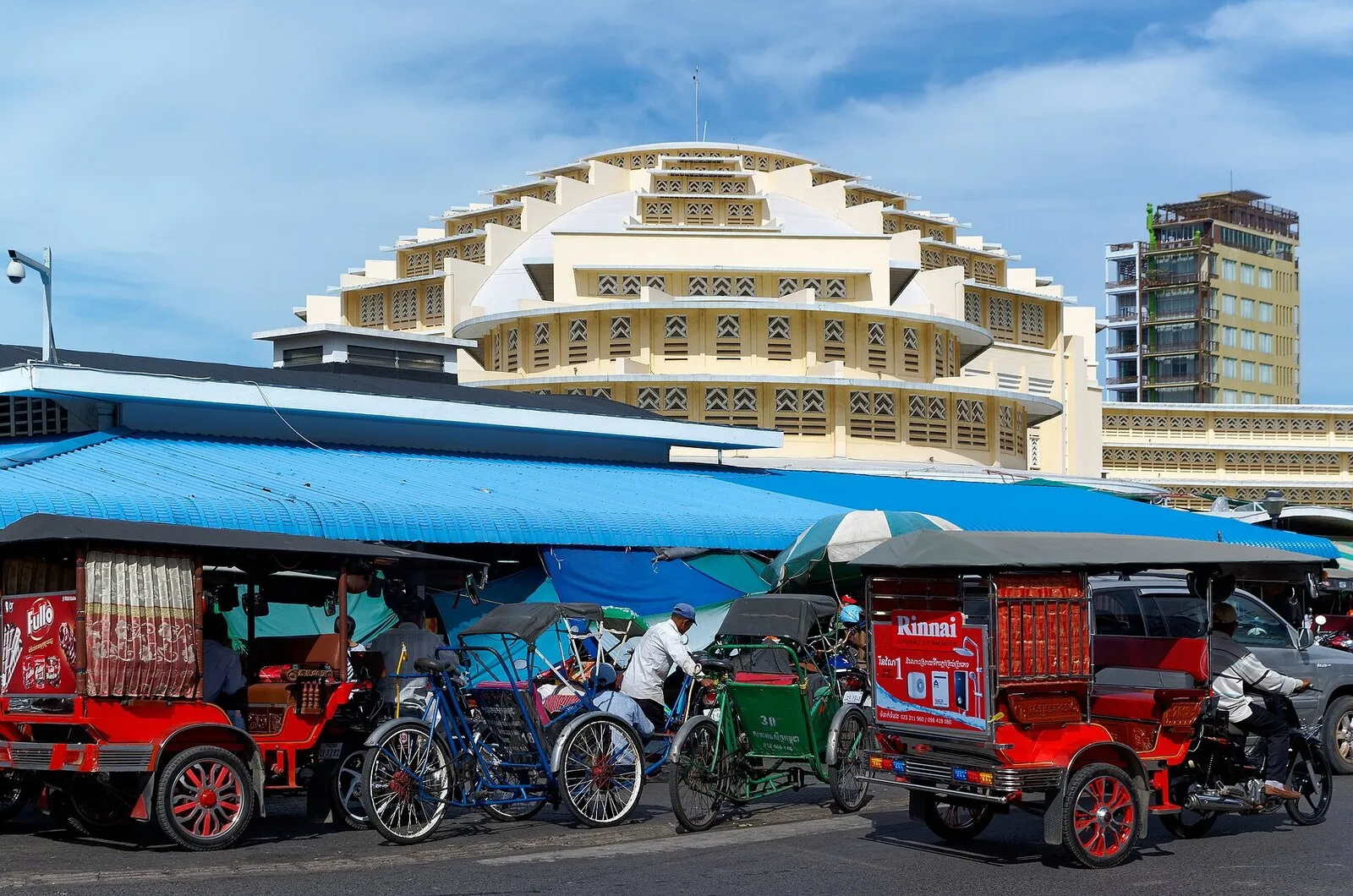 Żółta kopuła hali Central Market w Phnom Penh, przed nią tuk-tuki i riksze pod niebieskim zadaszeniem straganów