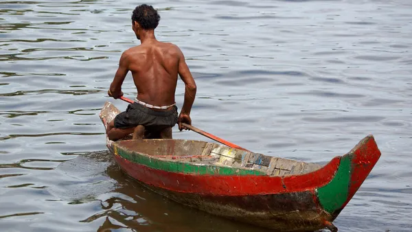 Rybak wiosłujący w drewnianej łodzi na jeziorze Tonle Sap