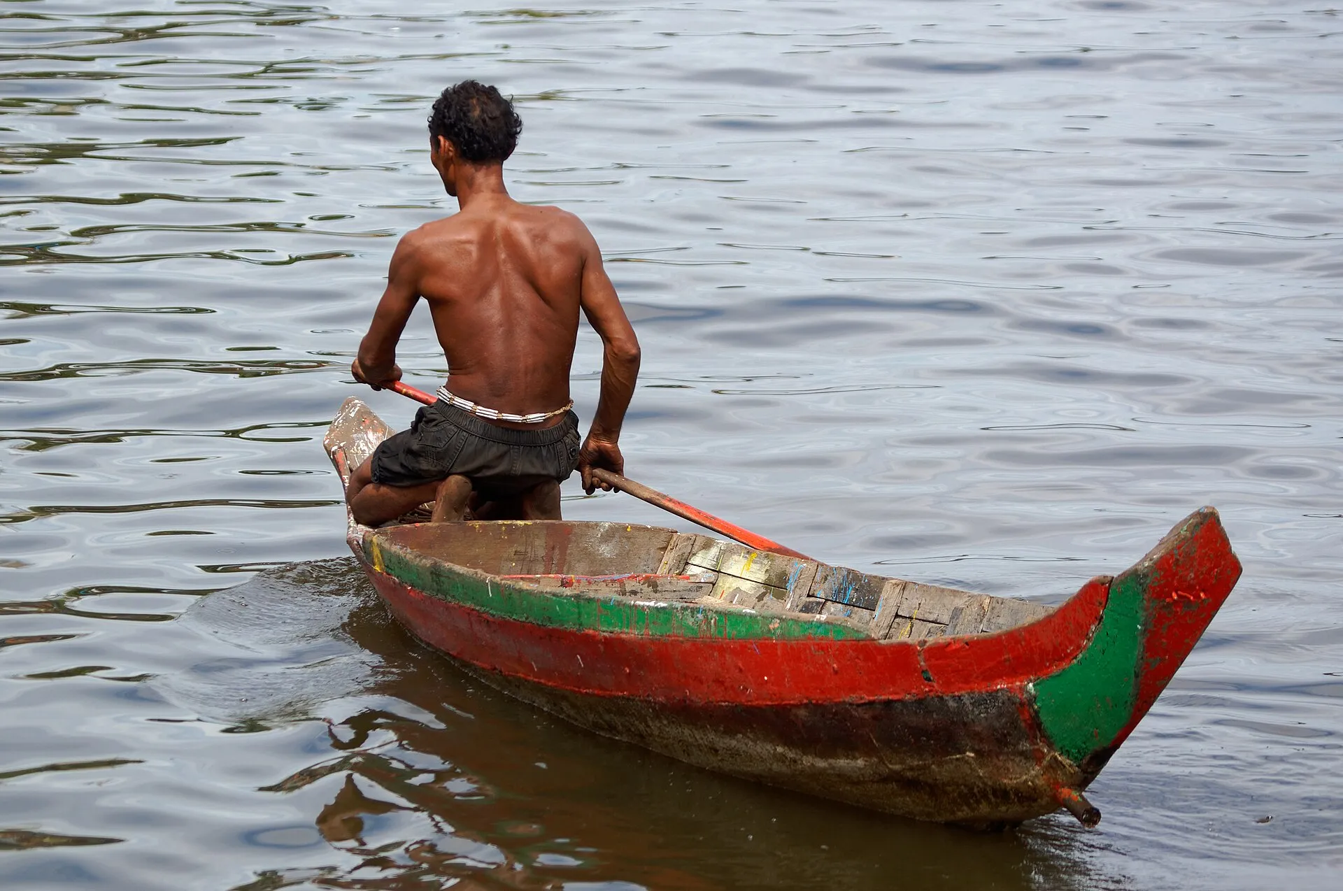Rybak wiosłujący w drewnianej łodzi na jeziorze Tonle Sap