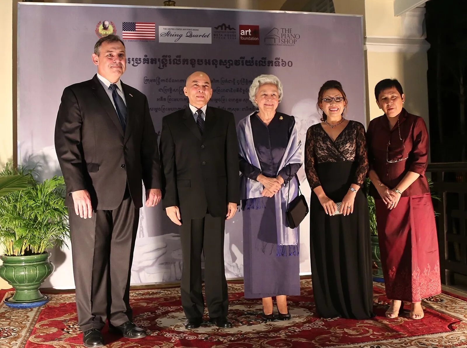 Król Norodom Sihamoni i królowa matka Norodom Monineath stoją w grupie gości przed planszą koncertu w Phnom Penh
