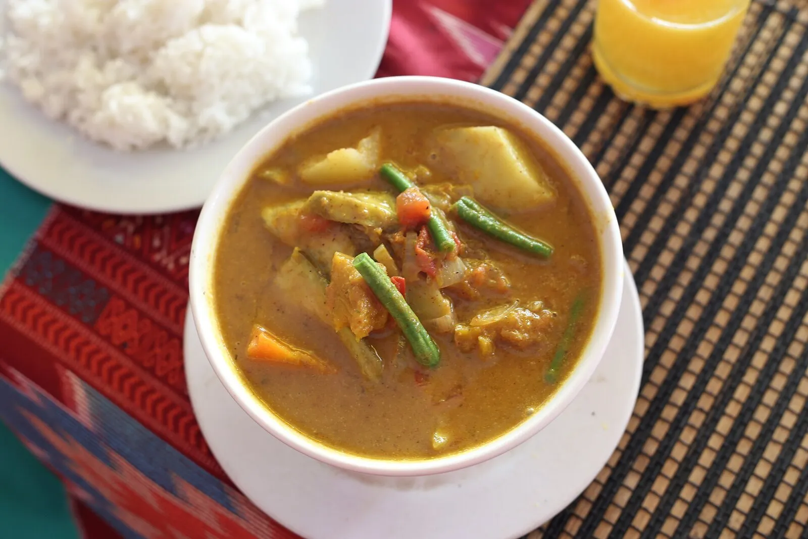 Kambodżańskie czerwone curry z ziemniakami, marchwią i fasolką szparagową w białej misce, obok ryż