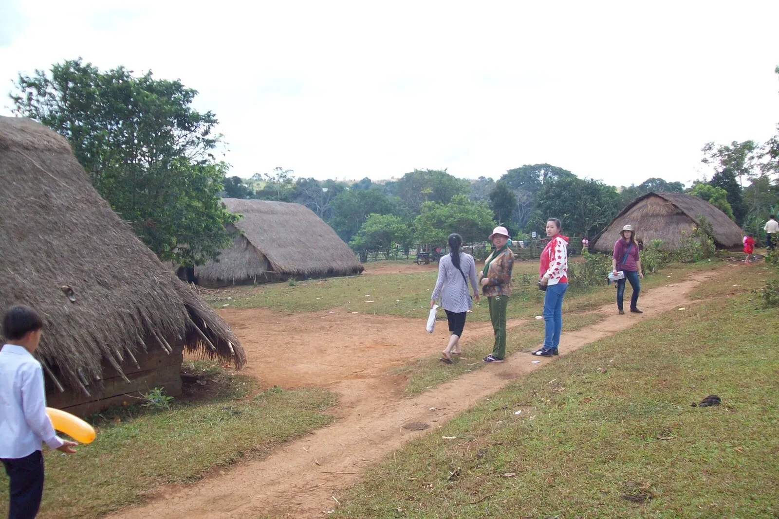 Chaty kryte strzechą sięgającą niemal ziemi i ludzie na gruntowej drodze w wiosce w Mondulkiri
