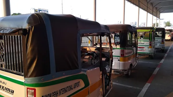Rząd tuk-tuków z napisem Phnom Penh International Airport na postoju przed lotniskiem