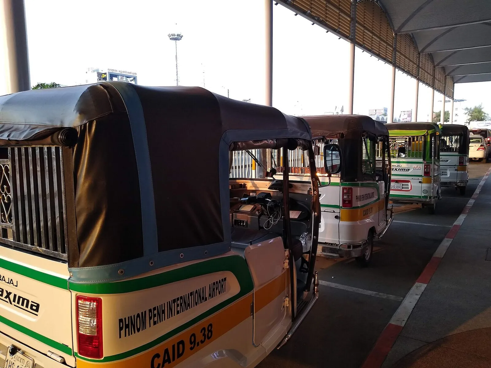 Rząd tuk-tuków z napisem Phnom Penh International Airport na postoju przed lotniskiem