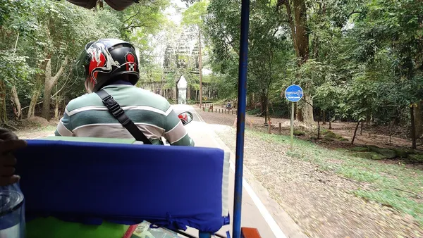 Widok z tuk-tuka na kierowcę w kasku i leśną drogę prowadzącą do bramy świątyni