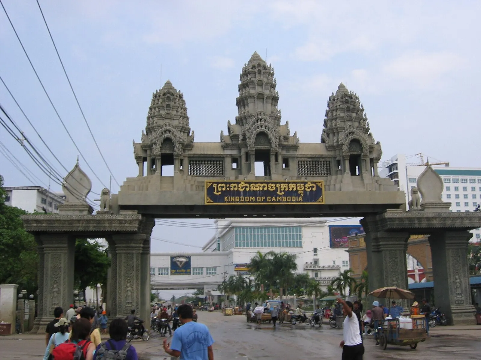 Brama graniczna w stylu khmerskim z napisem Kingdom of Cambodia na przejściu Poipet, pod nią piesi i riksze
