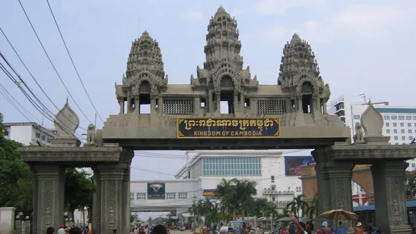 Brama graniczna w stylu khmerskim z napisem Kingdom of Cambodia na przejściu Poipet, pod nią piesi i riksze