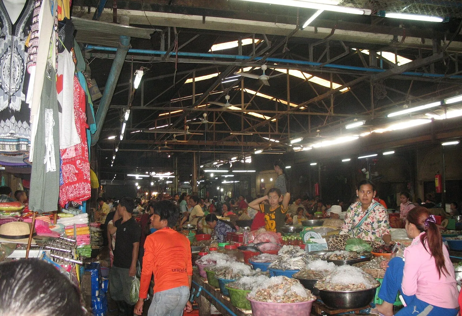 Wnętrze hali Old Market w Siem Reap: stragany z suszoną żywnością w miskach, sprzedawczynie i kupujący, z boku wieszaki z ubraniami