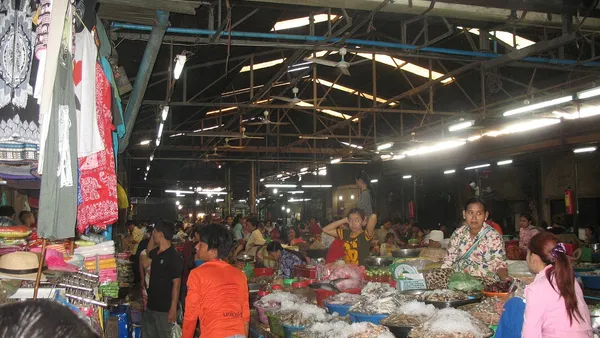 Wnętrze hali Old Market w Siem Reap: stragany z suszoną żywnością w miskach, sprzedawczynie i kupujący, z boku wieszaki z ubraniami