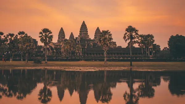 Pięć wież Angkor Wat i palmy na tle pomarańczowego nieba o świcie, odbite w wodzie stawu