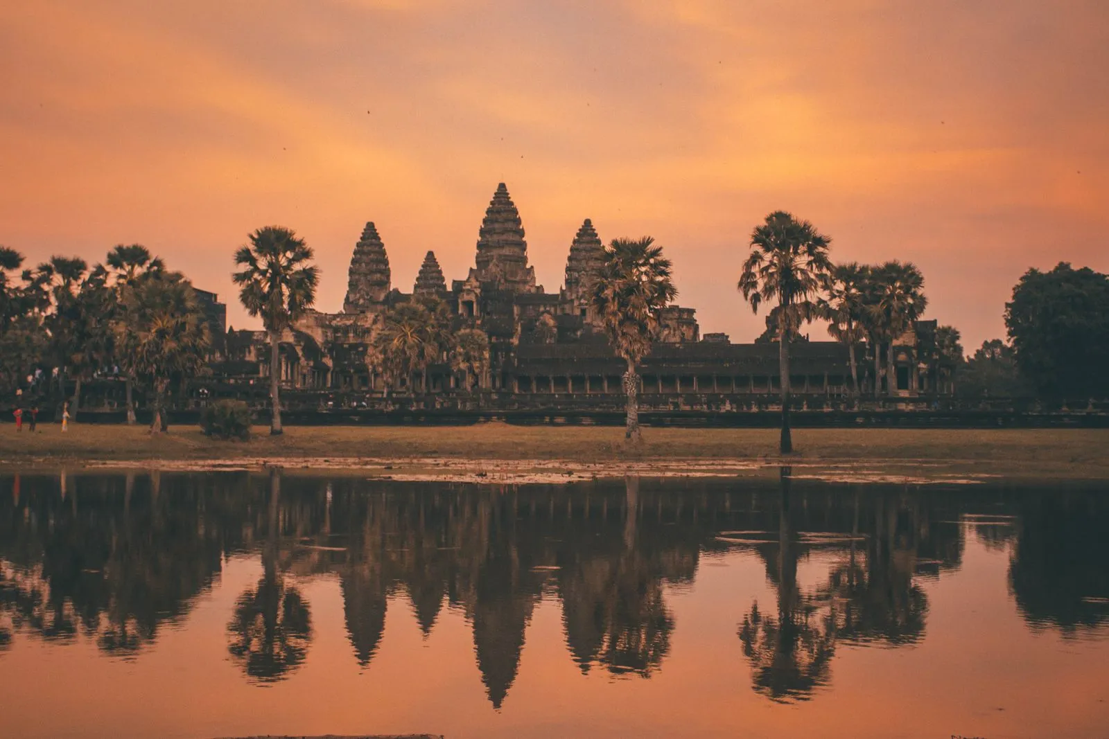 Pięć wież Angkor Wat i palmy na tle pomarańczowego nieba o świcie, odbite w wodzie stawu
