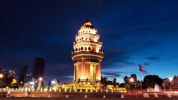 Podświetlony Pomnik Niepodległości w Phnom Penh po zmroku, obok fontanny i flaga Kambodży na maszcie
