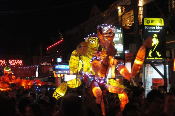 Podświetlone gigantyczne kukły niesione ulicą Siem Reap wieczorem